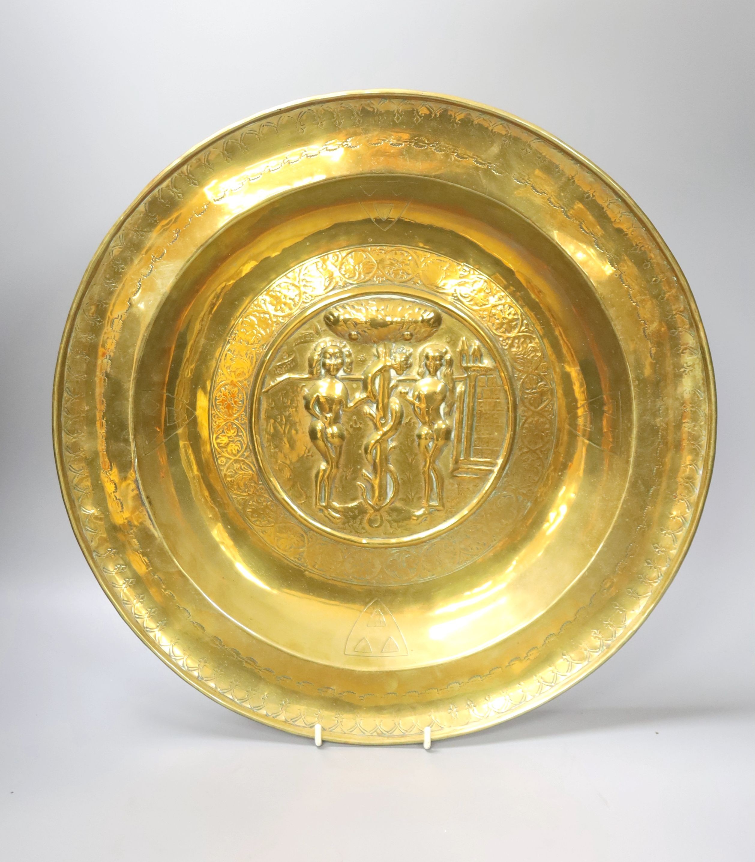 A large Nuremberg brass alms dish, 17th century, depicting Adam and Eve within a twisted foliate and floral border, with stylised armorial shields, 42cm